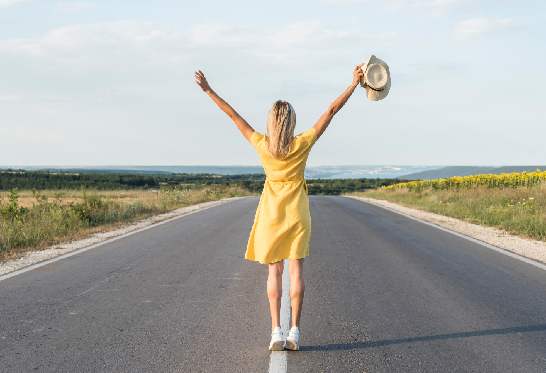 Femme de dos sur une route les bras tendus
